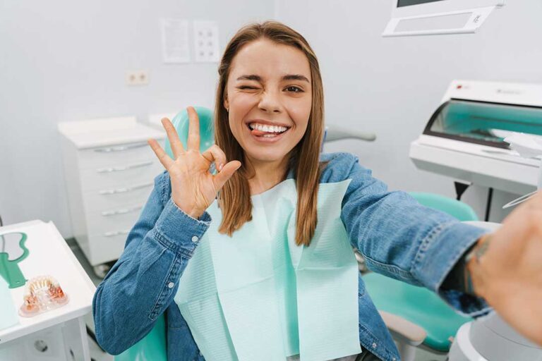 A dentist in blue gloves examining a child's teeth while a parent looks on in a bright dental office.